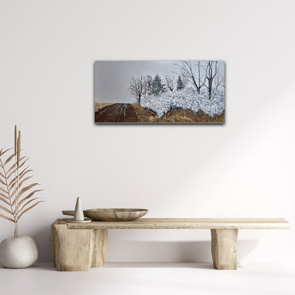 Oil painting of a winter landscape with trees and snow on a white wall above a wooden table.