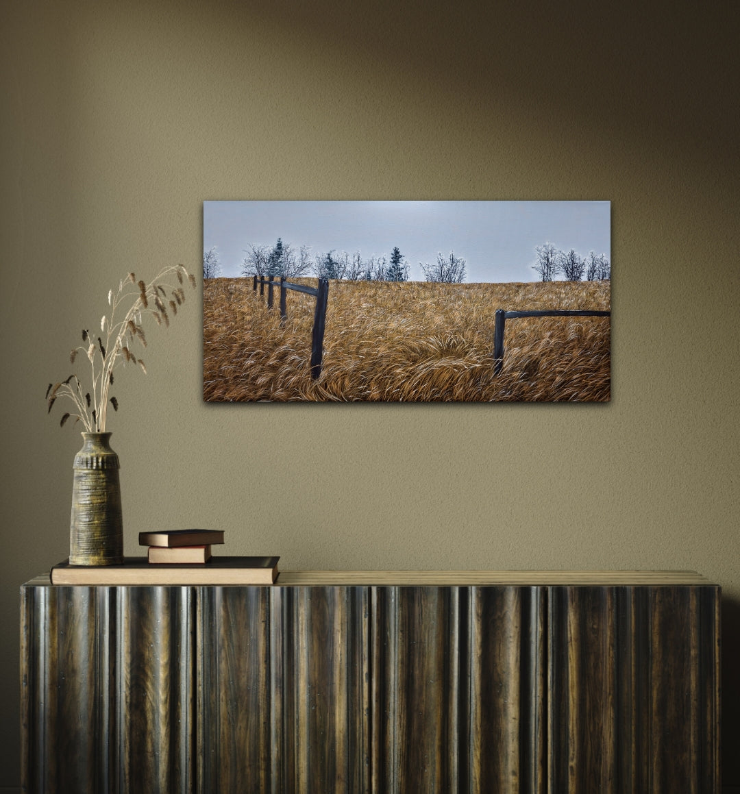 Framed landscape painting of a field with trees on a wall above a wooden console table.