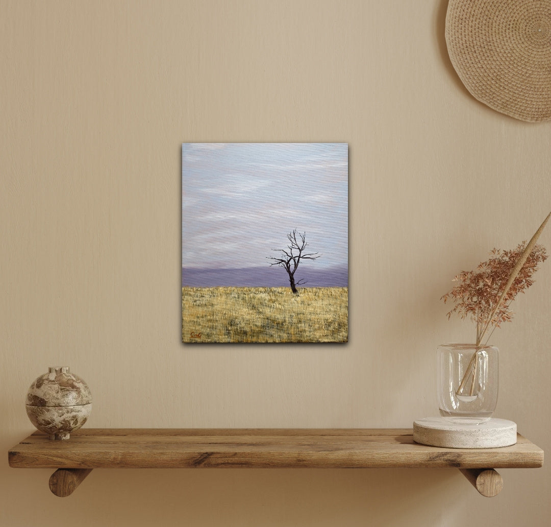 Change - 12"x10" oil landscape painting of a solitary winter tree in a hay field with the cold moving in on the horizon, on a yellow wall
