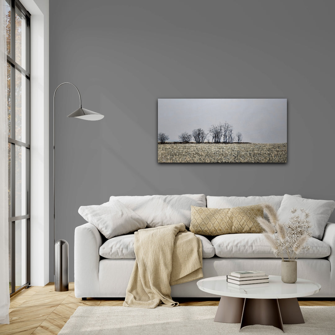 Finter 18"x36" oil painting of a field with winter trees and a blue-grey horizon on a blue grey living room wall behind a white couch