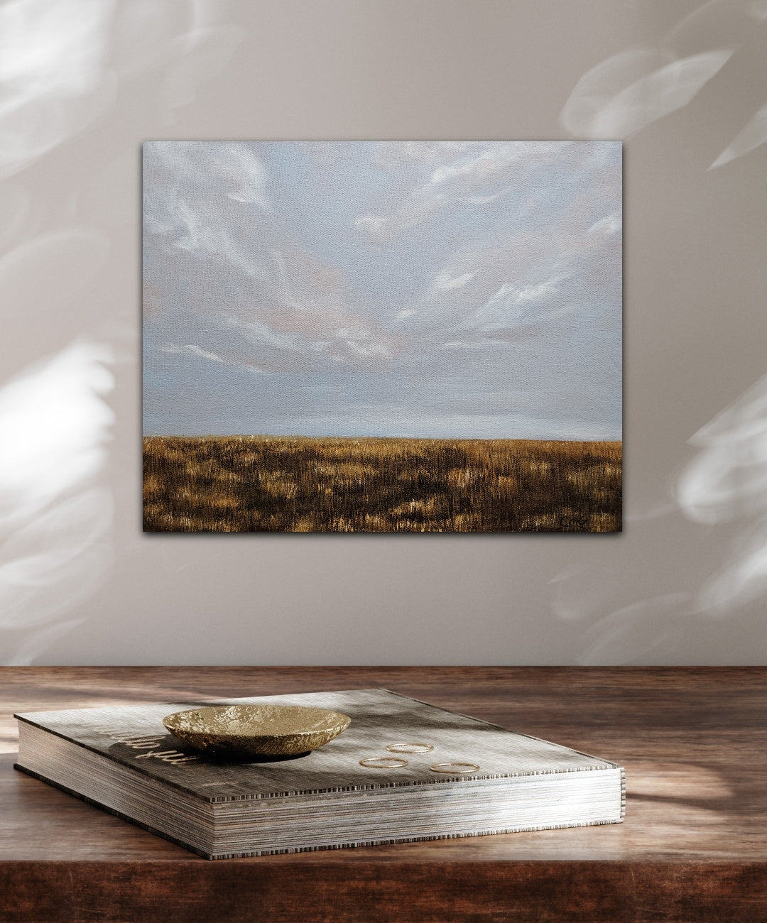 Breathe-oil landscape painting of a soft sky and flat prairie in fall all gold and brown hung over a wood desk