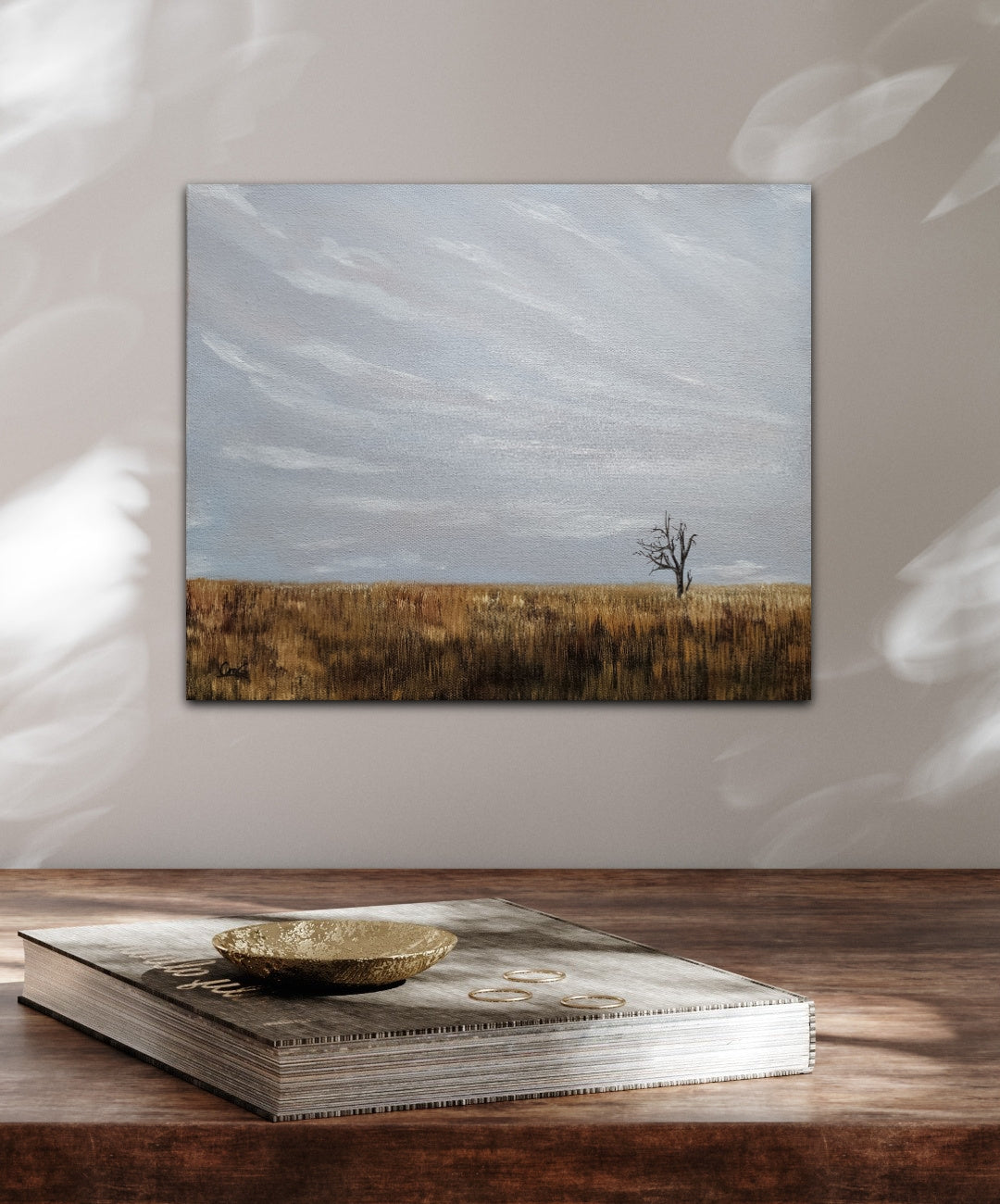  oil landscape painting of a single solo tree in a golden fall field under a grey/blue sky hung over a wood desk