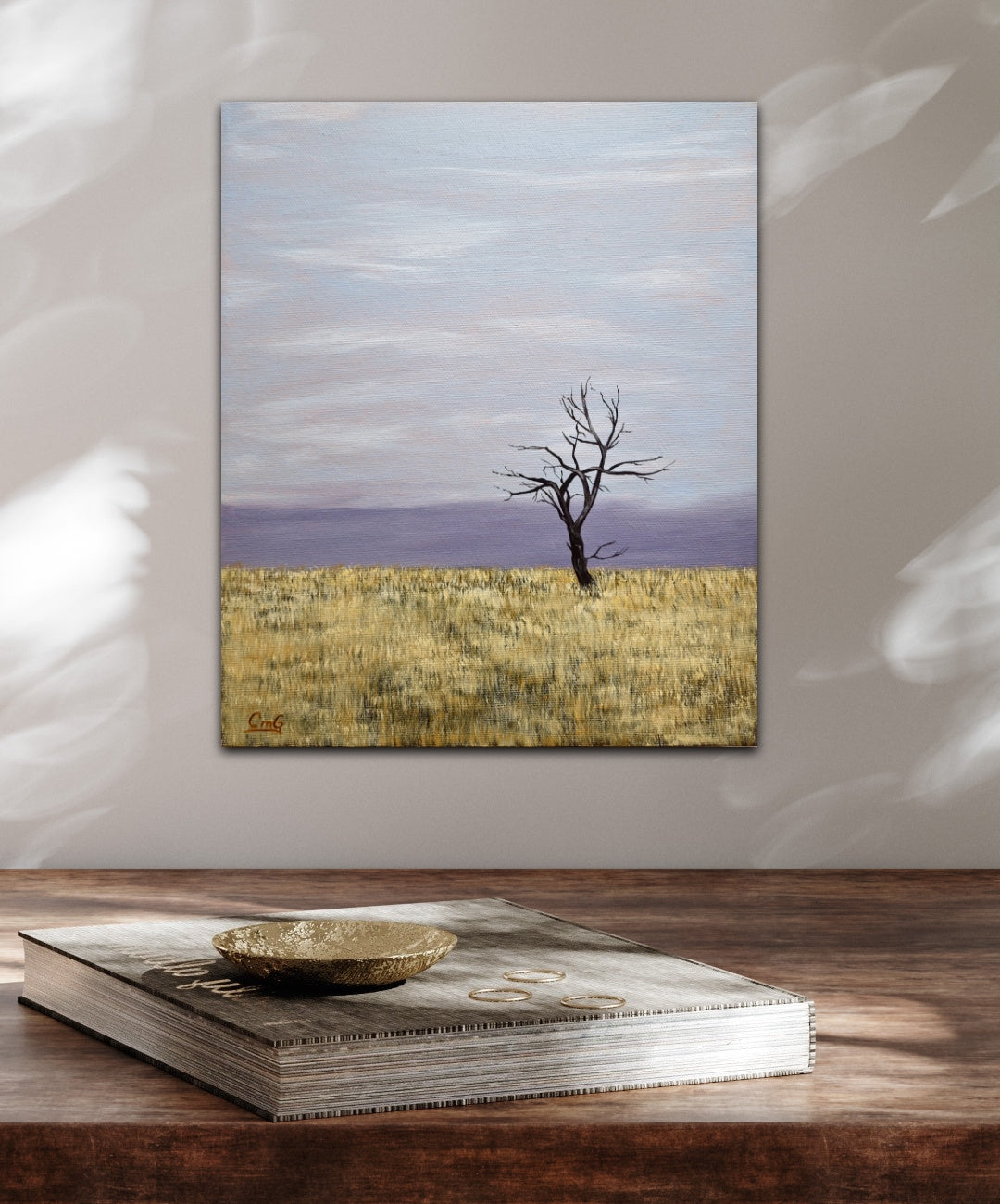 Change - 12"x10" oil landscape painting of a solitary winter tree in a hay field with the cold moving in on the horizon, over a wood desk