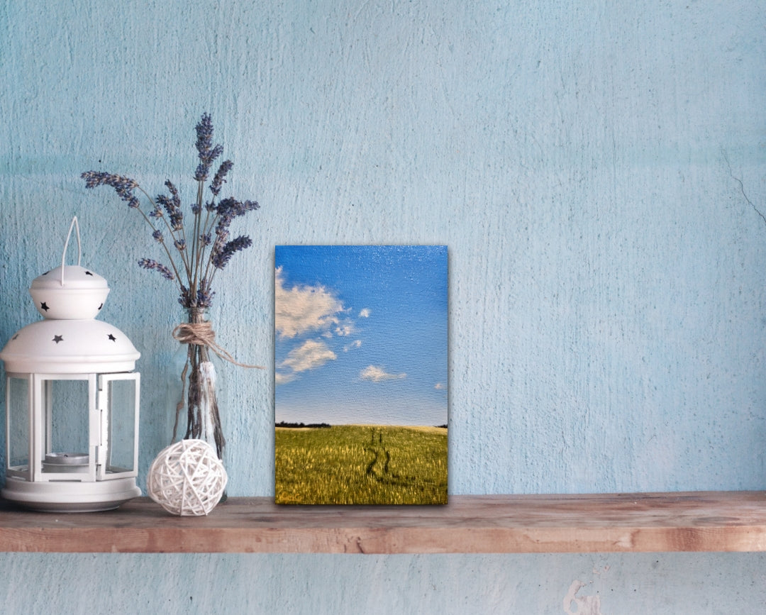 Decorative shelf with a lantern, vase with lavender, and a painting of a field on a blue wall.