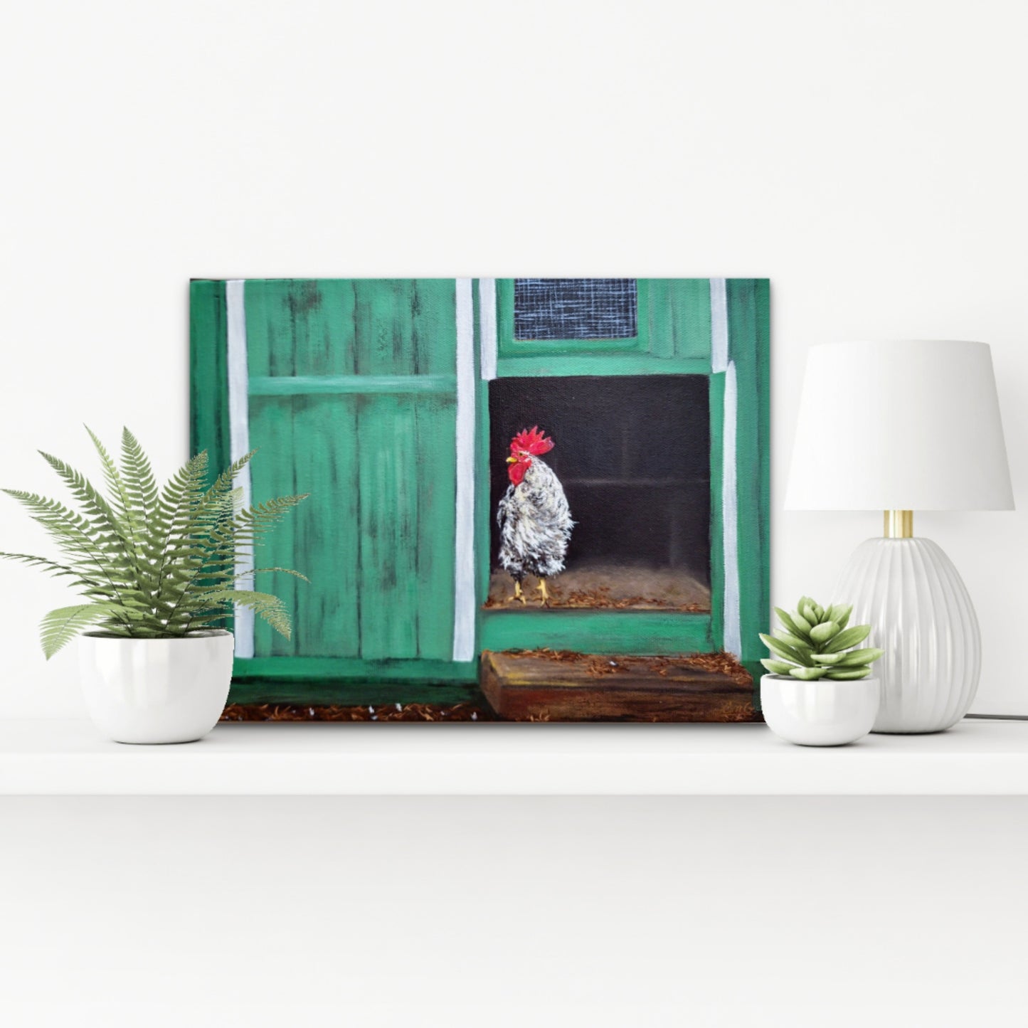 Decorative wall art of a rooster in front of a green door on a white surface with plants and a lamp.