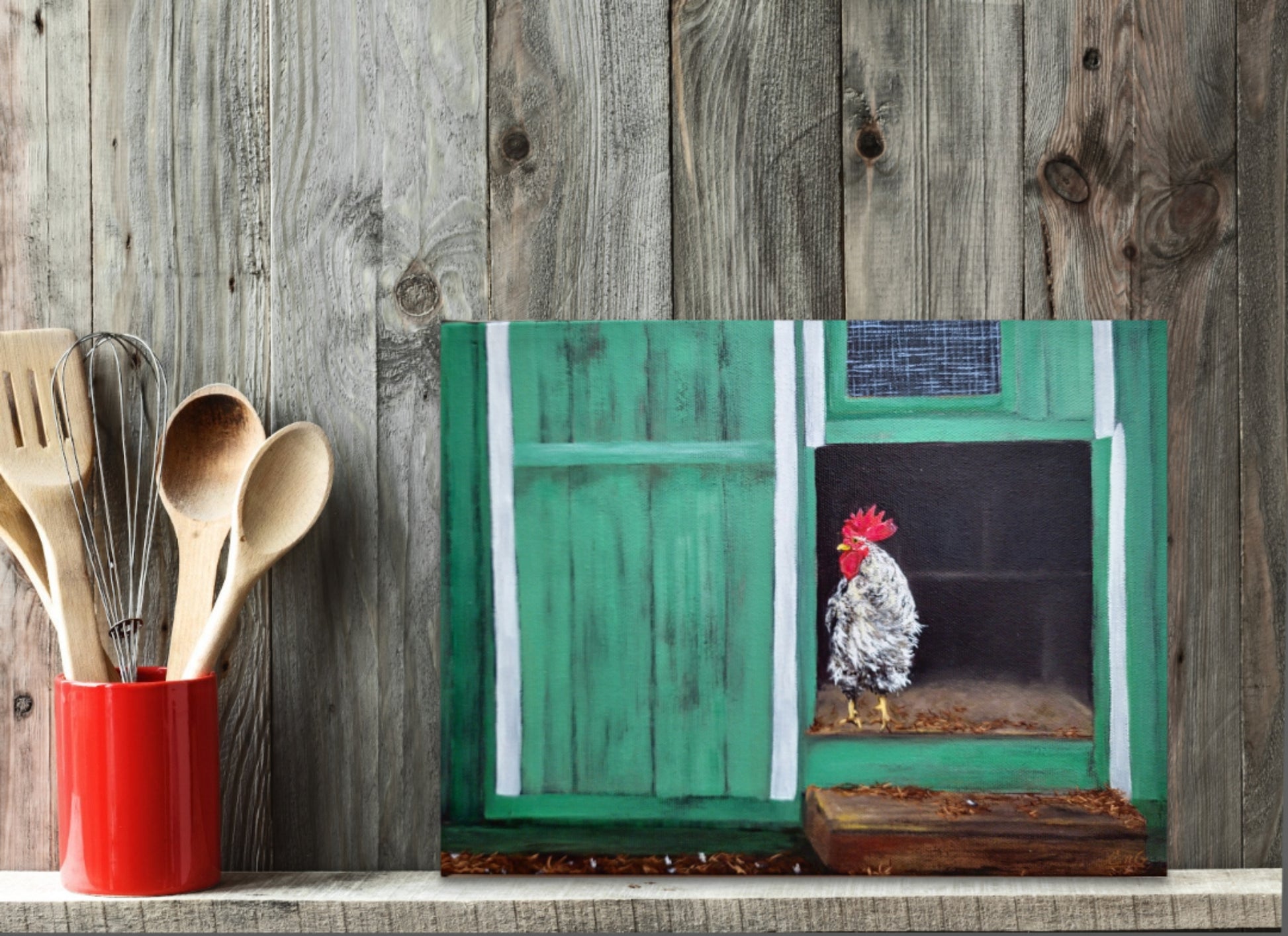 Wooden utensils in a red container next to a painting of a rooster in a green door.
