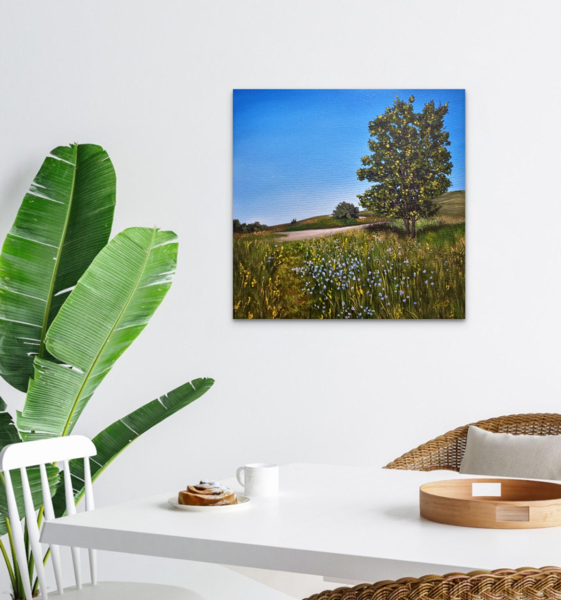 Surreal landscape painting on a wall above a table with a plant and coffee cup.