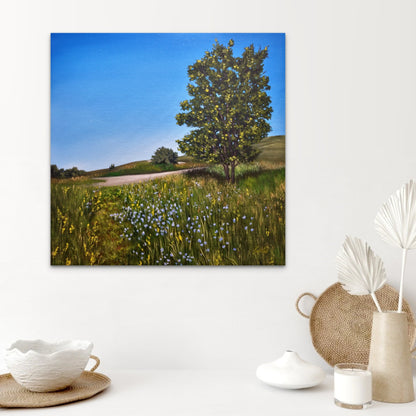 Scenic landscape painting of a tree in a field with decorative items below on a white surface.