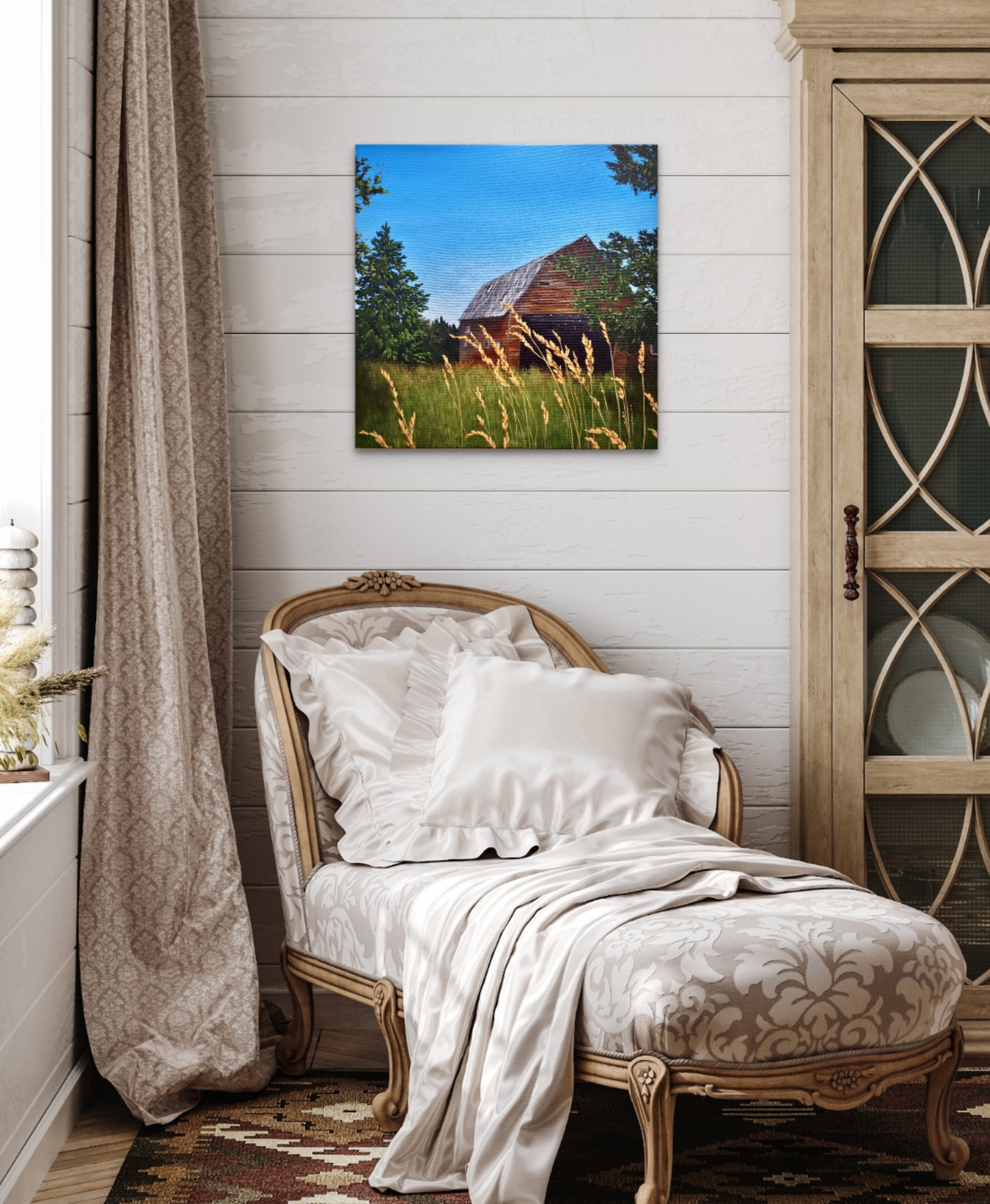 Decorative chair with white pillows and a blanket in a room with a painting of a barn on the wall.