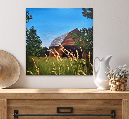Painting of a barn in a field on a wall above a wooden console table with decorative items.