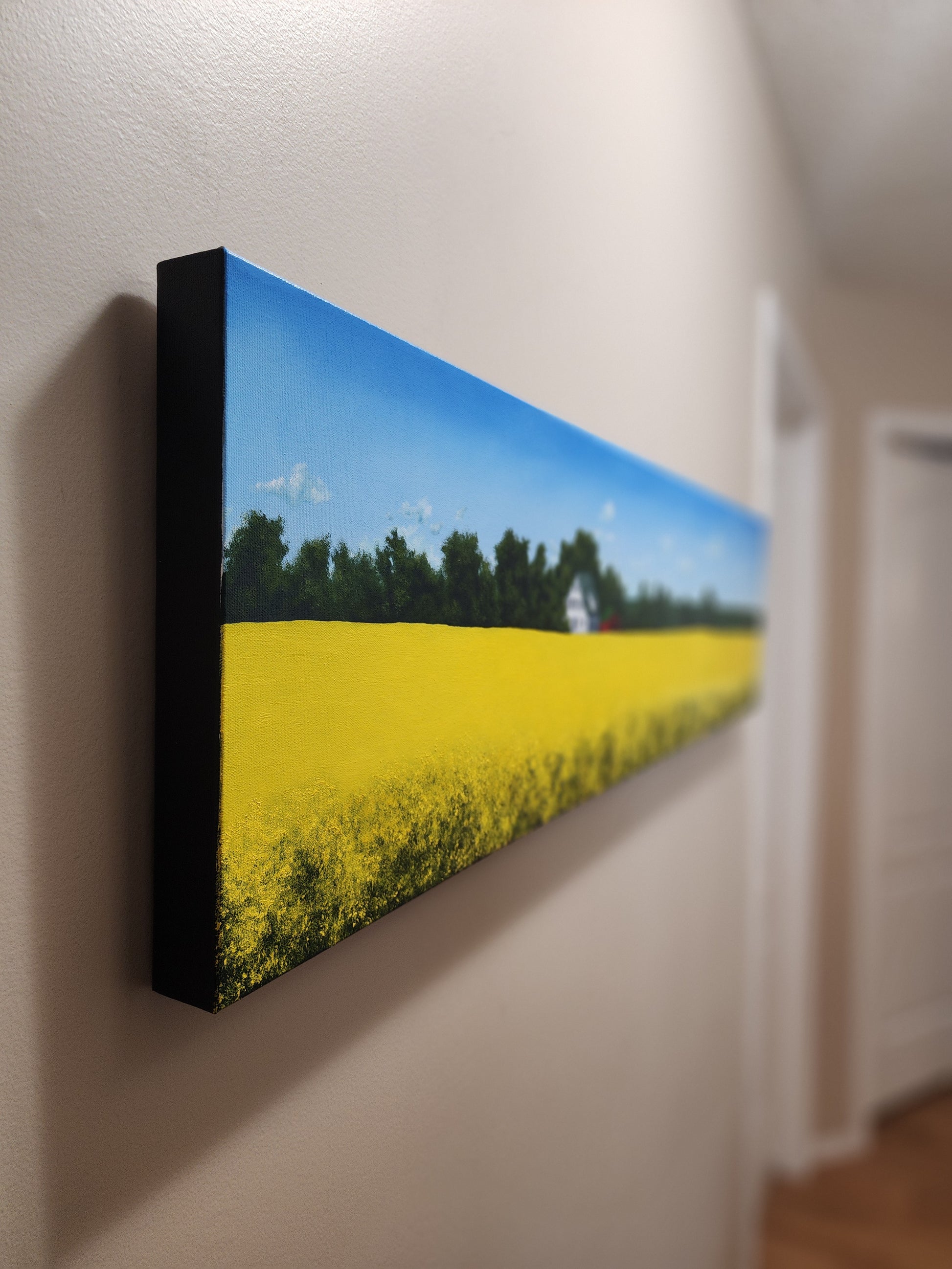 Rectangular oil painting with a landscape of a yellow field and blue sky.