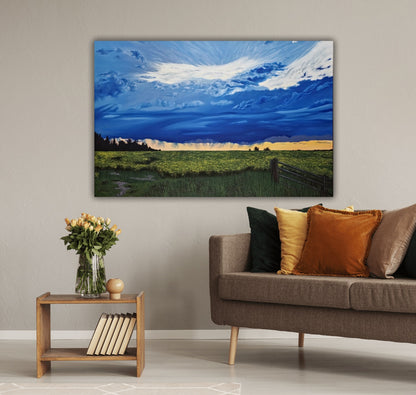 Canola Field At Dusk is an original oil painting of vibrant storm clouds over a beautiful sunset, over the prairie canola fields. Hanging on a wall behind a couch and table