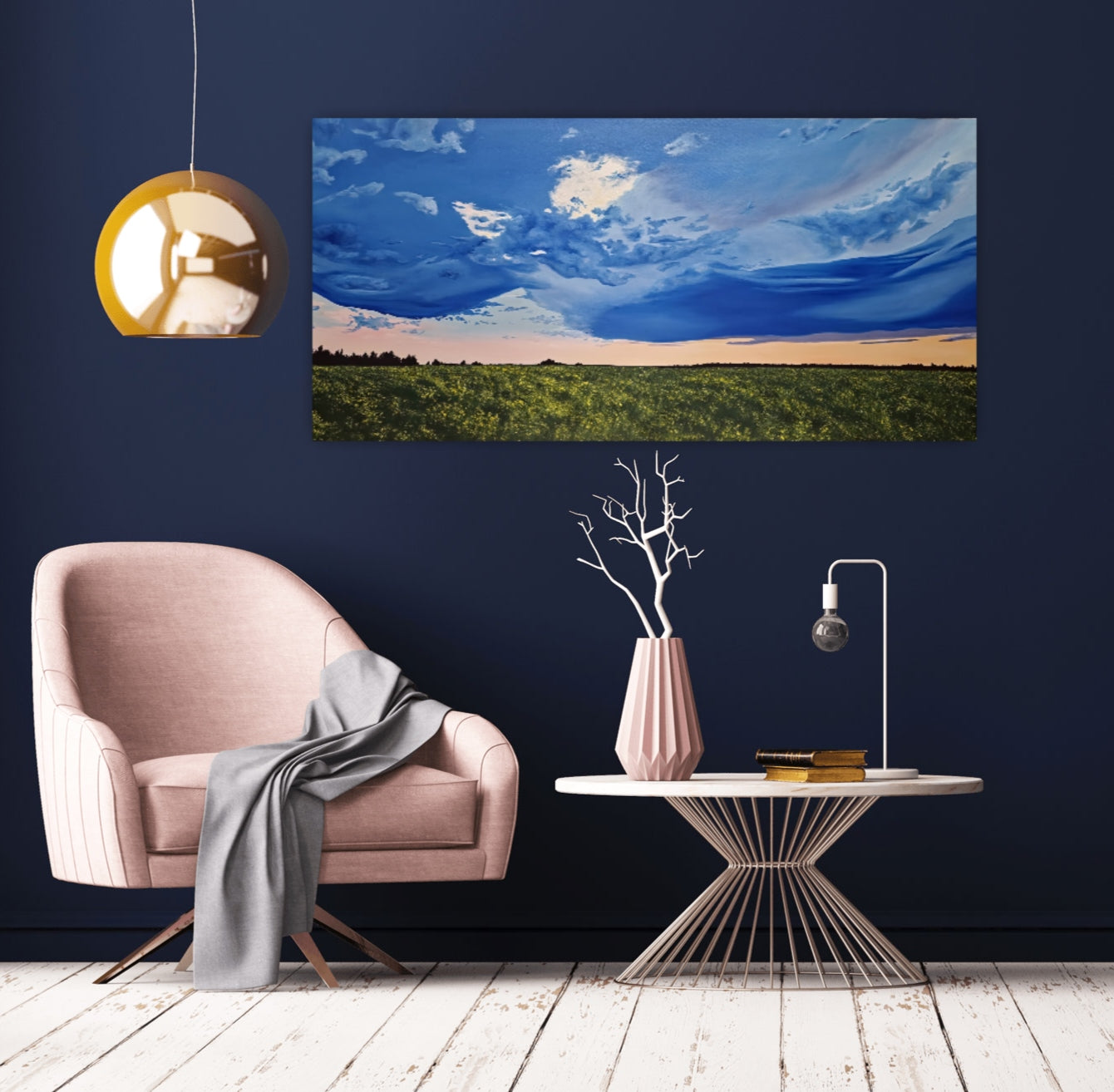 Golden Hour Affirmation is an original oil painting by Christina Gouldsborough of a vibrant stormy sky with a sunset over a canola field on a blue wall behind a gold lamp and pink chair